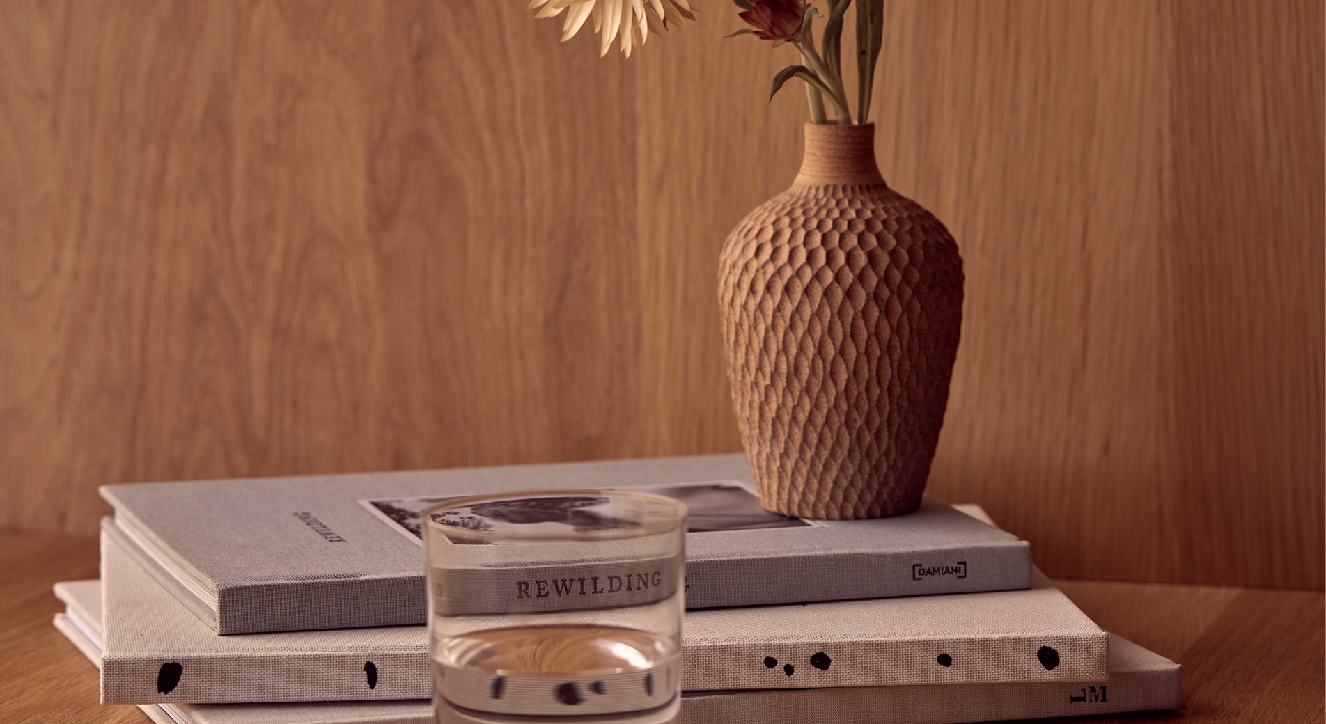 how to create a calming bedroom. close up of bedside table, with glass of water, three books and a vase with flowers.