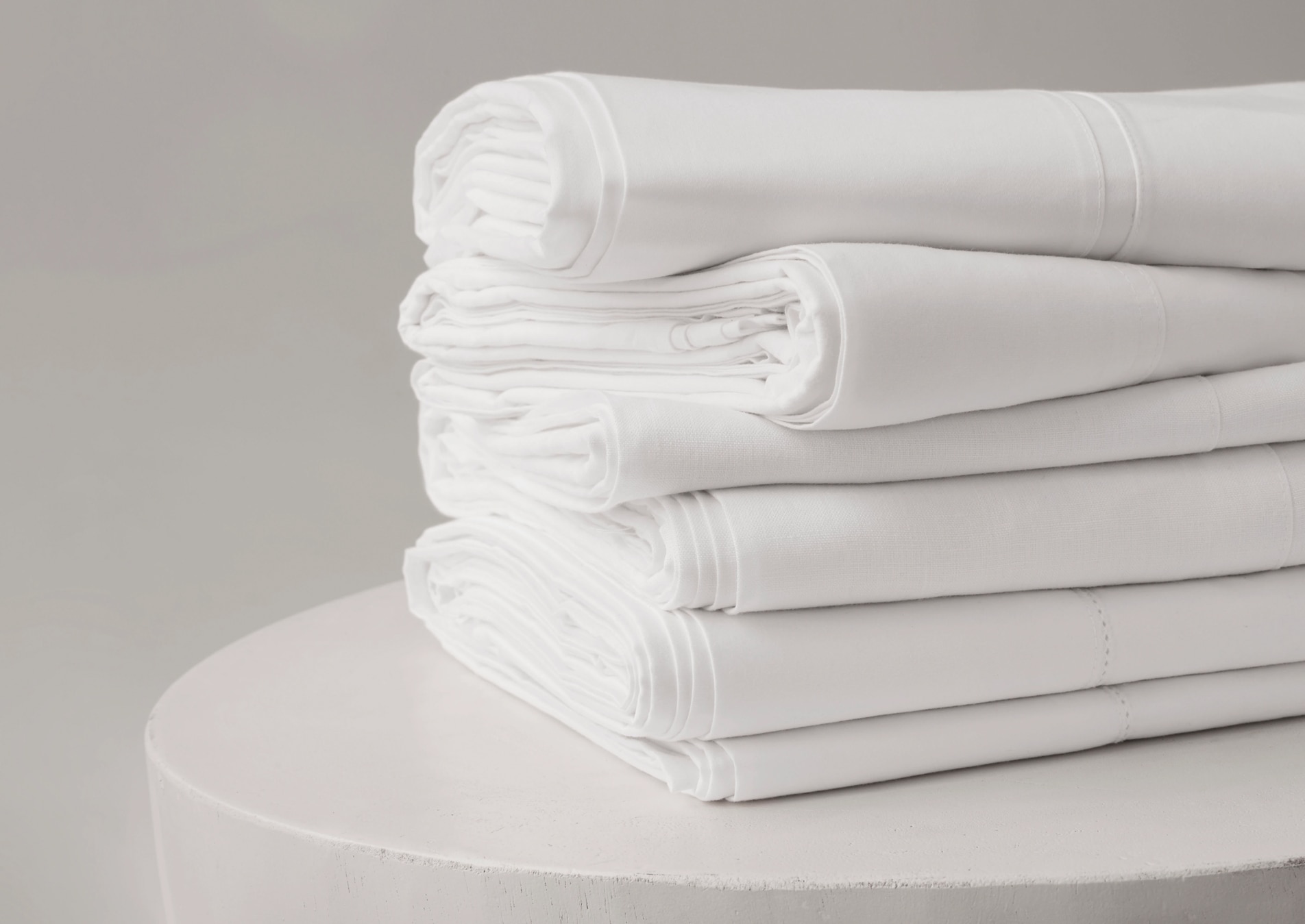 A pile of white sheets, folded and stacked on top of a white table